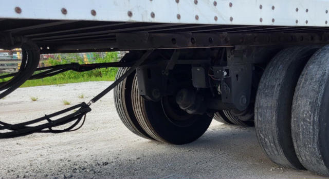 Trailer undercarriage showing dual axles and suspension components with tires, leaf springs, and hydraulic lines.