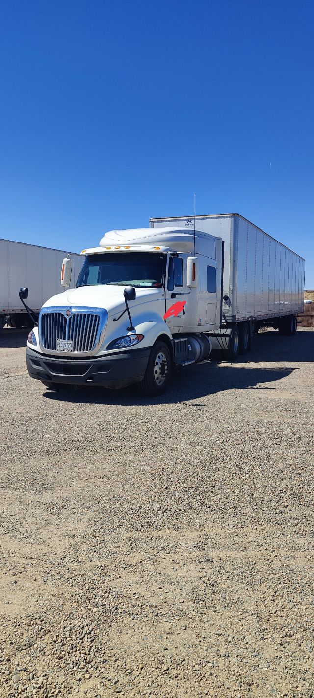 2016 International ProStar conventional sleeper truck with a long white trailer, front grille visible, in a gravel lot.