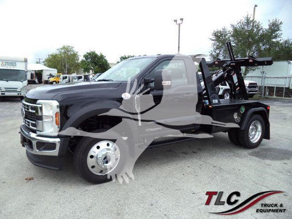 2024 Ford F450 tow truck front-left view with wheel and towing equipment in rear, TLC Truck & Equipment watermark bottom right, faint dealership lot in background.