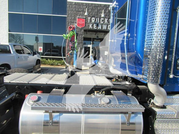 Kenworth W900L truck cab and chrome fuel tanks, side view showing steps and blue cab in a dealership lot.