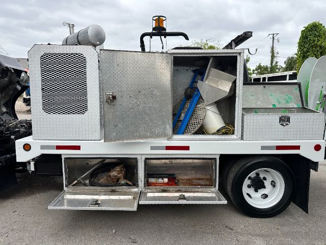 GMC W5500 utility truck storage compartments with aluminum toolbox doors and equipment inside, side view showing rear compartments and wheel.
