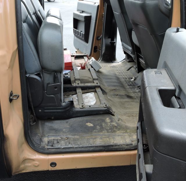 Ford F-350 crew cab interior with missing front seat rails, exposed floor, and utility equipment in rear; dirt and wear on the rubber floor mat.