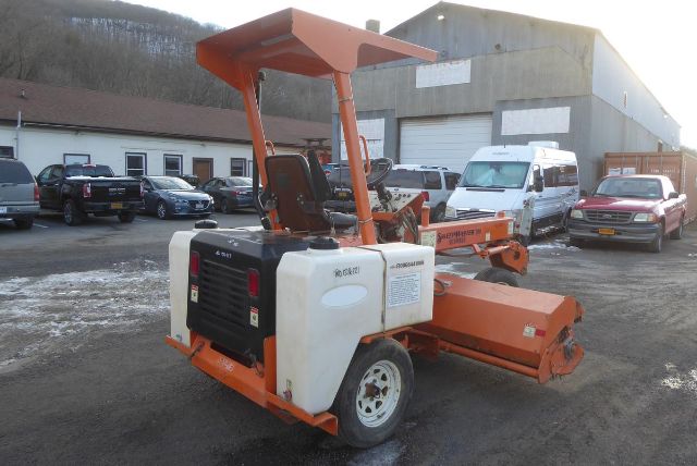 Laymor SM300 compact road roller with white fuel tanks and orange frame, operator seat, and roller drums in an outdoor lot.