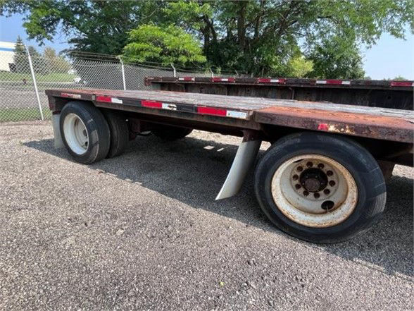 Flatbed trailer with dual rear wheels and wooden deck, showing wheel rims and fender clearance.