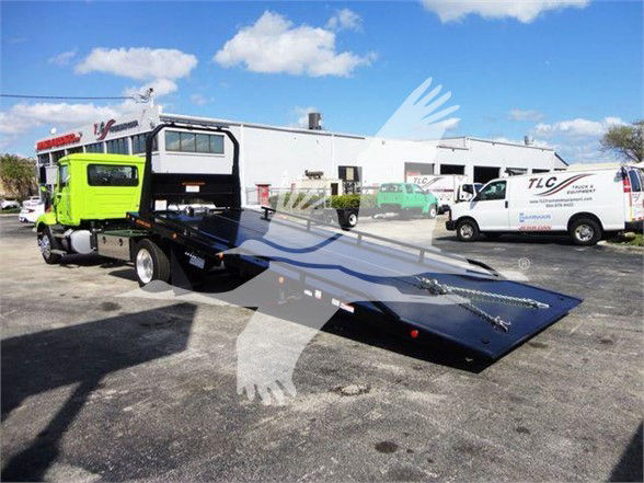 MD6 tow truck with a bright green cab and a flatbed in a parking lot; other service vans in background under blue sky.