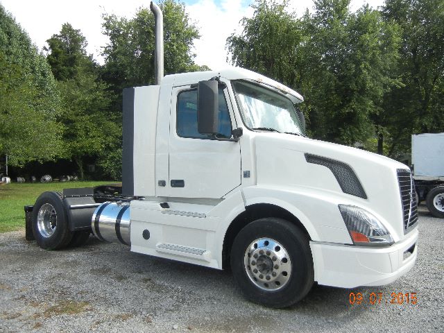 Volvo VNL42300 cab over style truck shown in white with side steps, chrome fuel tanks, and a vertical exhaust stack.