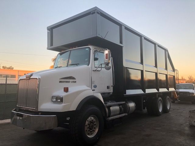 Dump truck with a large black dump body and white cab, five visible wheels, Western Star logo on the radiator area, in-service condition.
