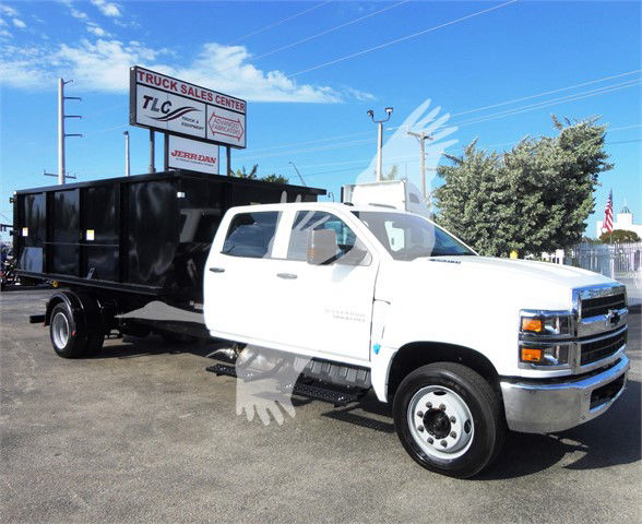 2023 Chevrolet Silverado 5500HD truck with white cab and black dump body, front three-quarter view in dealership lot.
