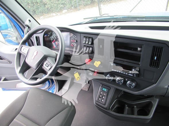 Kenworth truck interior photo showing steering wheel with Kenworth logo, dashboard with gauges, central controls, gear shifter area, and dashboard panels.