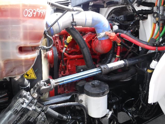 Engine bay of a 2018 International 4300 flatbed truck showing red engine, blue intake hose, coolant reservoir, hoses, and wiring.