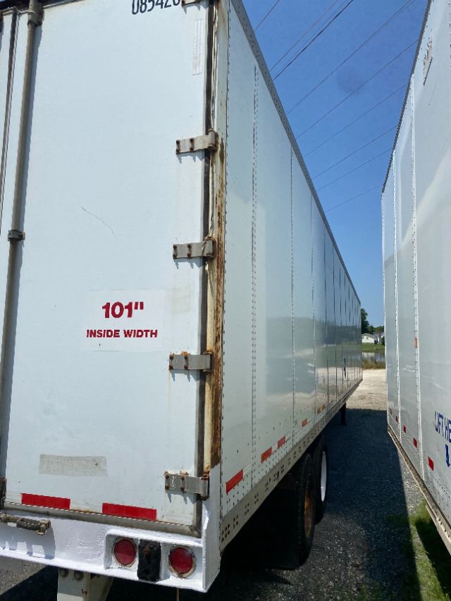 Rear left side of a white 101" inside width Wabash Duraplate trailer showing rear doors hinges and taillights.