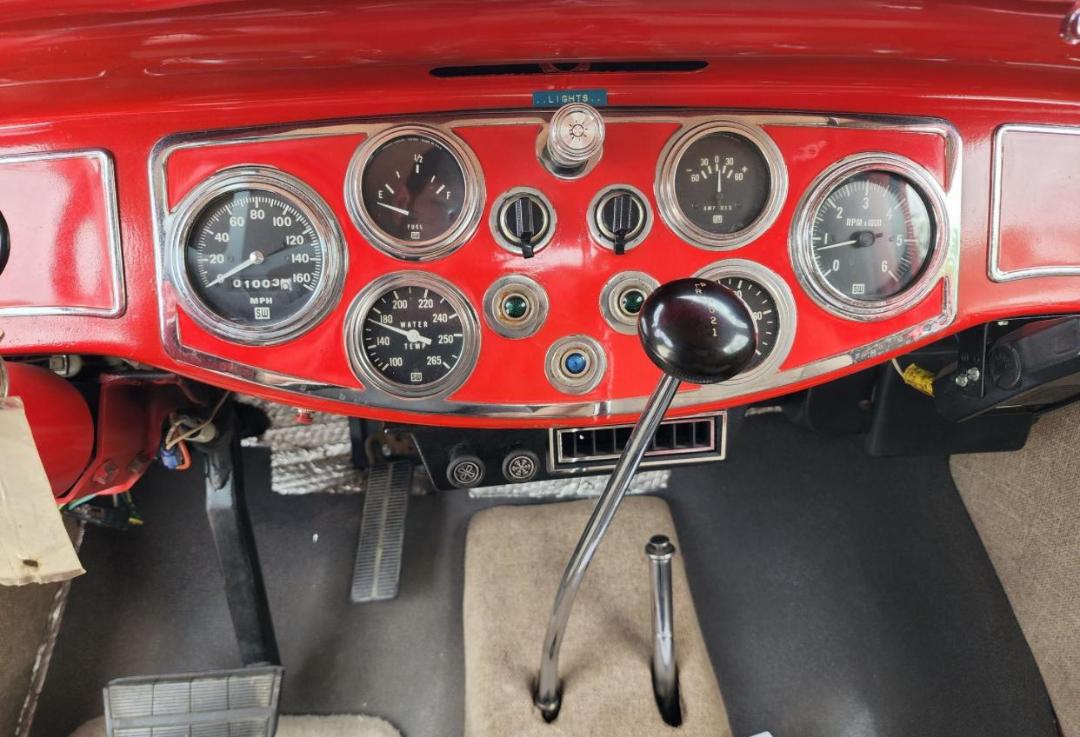 Dashboard of a red Diamond T hauler truck showing classic round gauges, analog speedometer, tachometer, fuel gauge, and a long gear shifter.