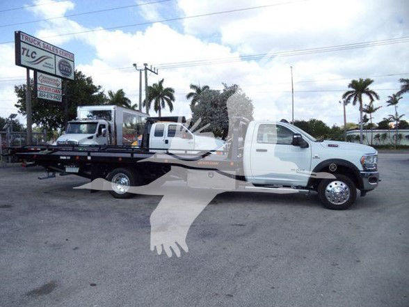 2024 Ram 5500 SLT tow truck in a dealership lot with a long flatbed, side view showing front cab and extended bed.