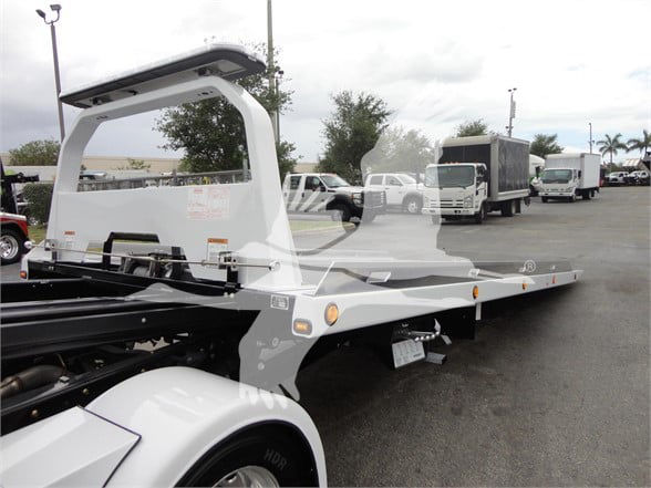 Flatbed tow truck with long aluminum deck and hydraulic tilt; Ram 5500 chassis visible; no legible text on side in view.
