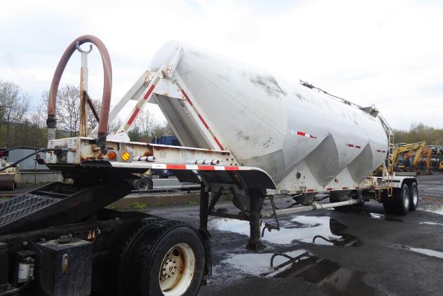 Fruehauf dry bulk pneumatic trailer on a trailer yard, silver cylindrical tank with diamond-pattern sides, rear wheels, and towing hitch.