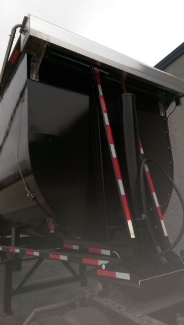 Dump trailer rear showing round bottom dump mechanism with hydraulic cylinders and support frame.