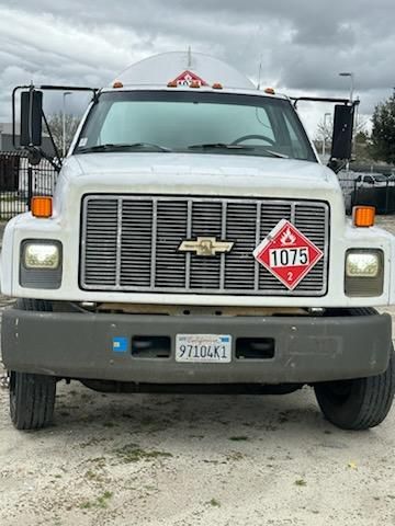 Front view of a white 1991 Chevrolet Kodiak truck with a large chrome grille, amber turn signals, and a hazardous material placard on the front bumper reading 1075. License plate visible. Side mirrors extend outward.