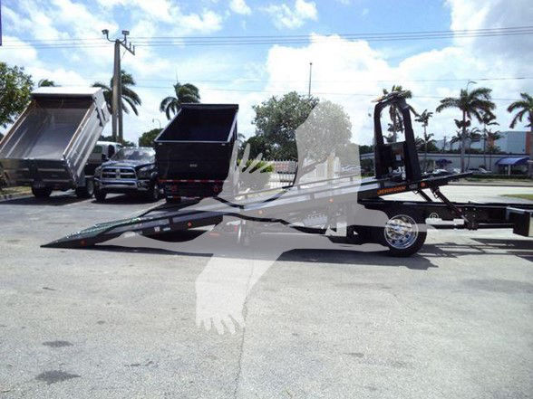 Tow truck trailer with a ramp and hydraulic system in a parking lot.