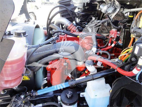 Truck engine bay with various hoses, cables, and a red-painted component. Visible are coolant reservoir, coolant hoses, and wiring harnesses in a dense engine compartment.