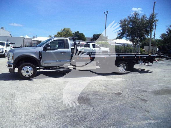 Ford F-600 dual rear wheels flatbed tow truck with extended cab and stake bed in a dealership lot.