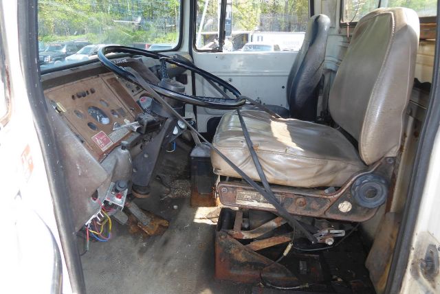Cab and chassis interior of a 1978 Ford 8000 showing steering wheel, dashboard with gauges, two seats, and exposed metal floor; worn tan seat upholstery.