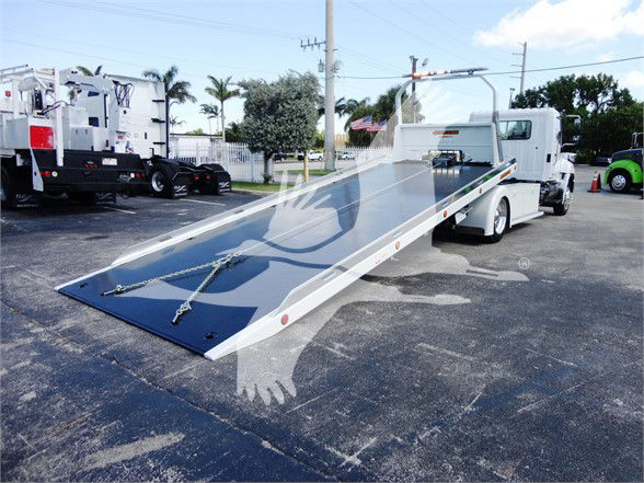 Flatbed tow truck with a lowered blue ramp bed and white cab, showing a long tilt-bed layout.