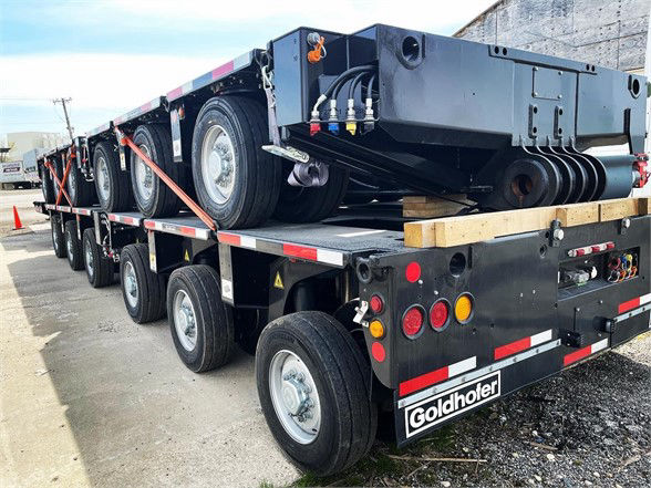 Goldhofer trailer with multiple axles and a flatbed, showing a spare beam and hydraulic connections on the front. The Goldhofer logo is visible on the rear right.