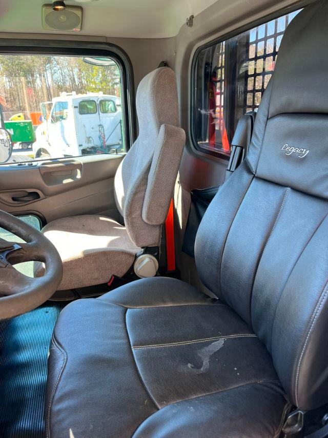 Cab interior of a 2016 Peterbilt 348 with gray fabric seats, driver seat and passenger seat, dashboard, window view showing a rollback truck outside.