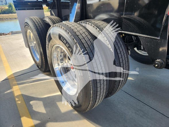 Two dual tires on a trailer axle with polished rims; text on tire sidewall includes 'MR2' or 'M+' and tread patterns visible.