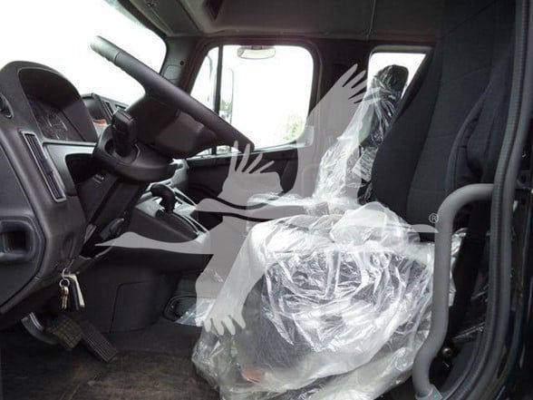 Truck cab interior driver seat with protective plastic cover showing steering wheel and dashboard of a Freightliner M2 106.