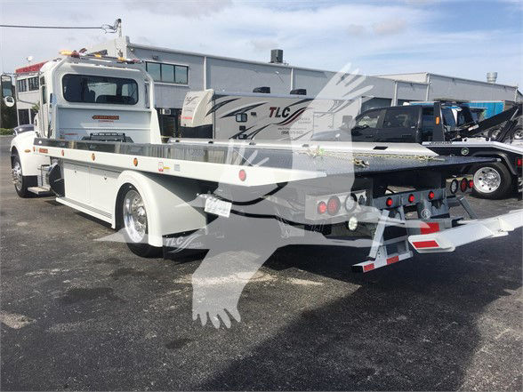 Peterbilt 337 tow truck flatbed in a dealership lot from rear left side showing winch, hydraulic bed, and rear lights.