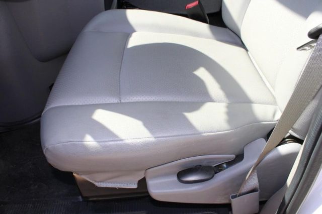 Ford E-450 front seat area showing light gray cloth seat with manual seat adjustment lever and seatbelt buckle.