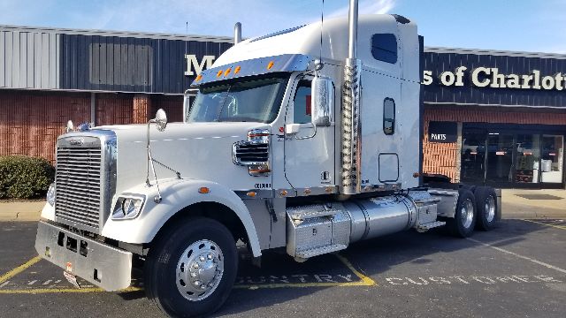 Conventional sleeper truck from 2013 Freightliner Coronado 132 in a light silver color, side view with chrome fuel tanks and dual rear axles.