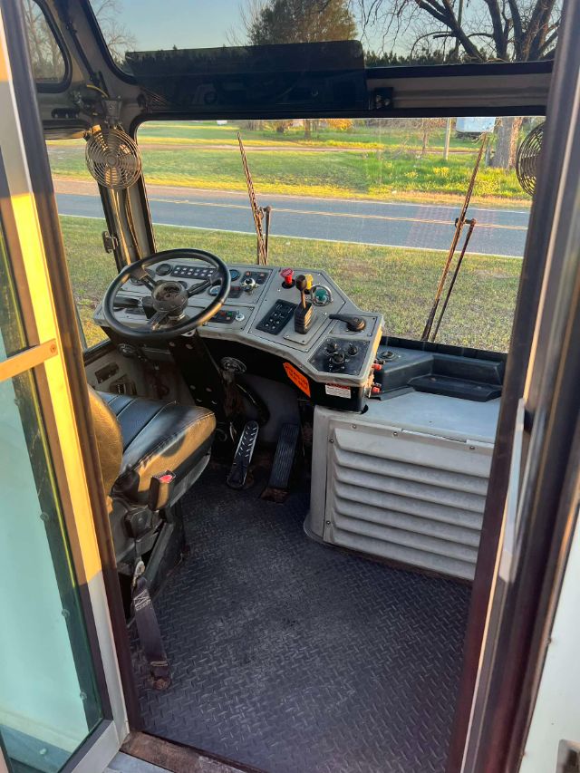 Operator cabin of a 2014 Tico Prosper? utility vehicle showing a steering wheel, dashboard with controls, pedals, and large side vents; front windshield and exterior world visible.