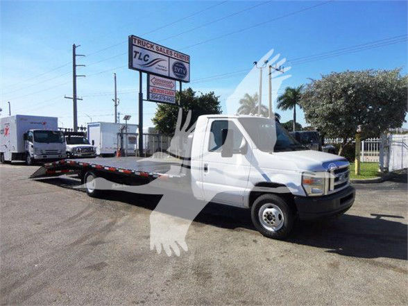 Flatbed tow truck 2011 Ford E450 with white cab and black chassis, long flatbed in a dealership lot.