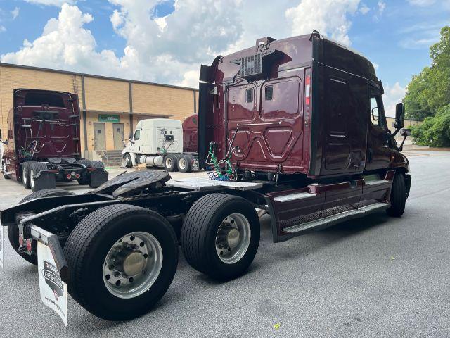 Truck chassis and cab of a maroon Freightliner Cascadia tractor in a parking lot showing rear wheels and attached sleeper area.