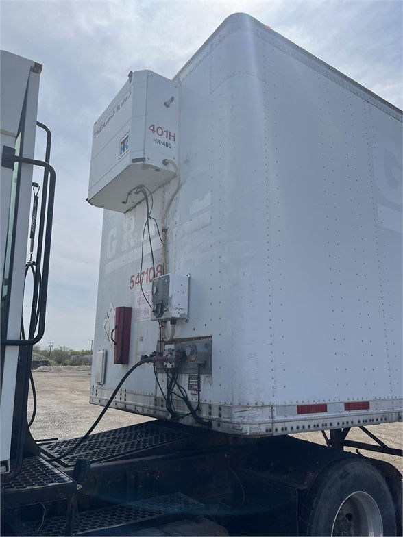 Rear of a white Wabash dry van trailer with a refrigeration unit mounted on front-left side; visible are electrical and service connections, coiled cables, and a lower door area.