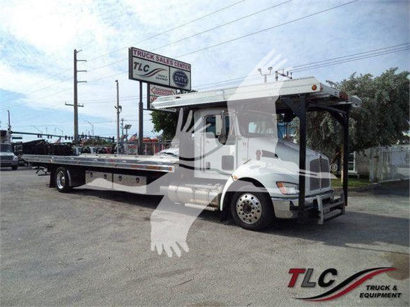 Kenworth T370 tow truck with flatbed in a dealer lot showing TLC Truck & Equipment logo.