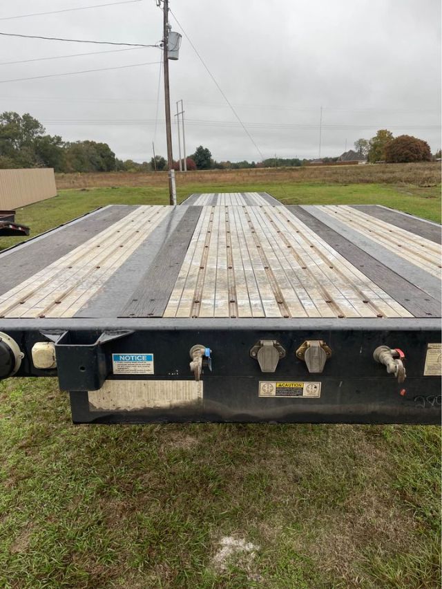 Flatbed trailer rear deck showing metal plank decking with warning labels and hitch connections.