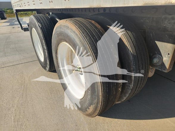 Trailer with dual rear axles showing two rubber tires and wheel rims under a flatbed trailer frame.