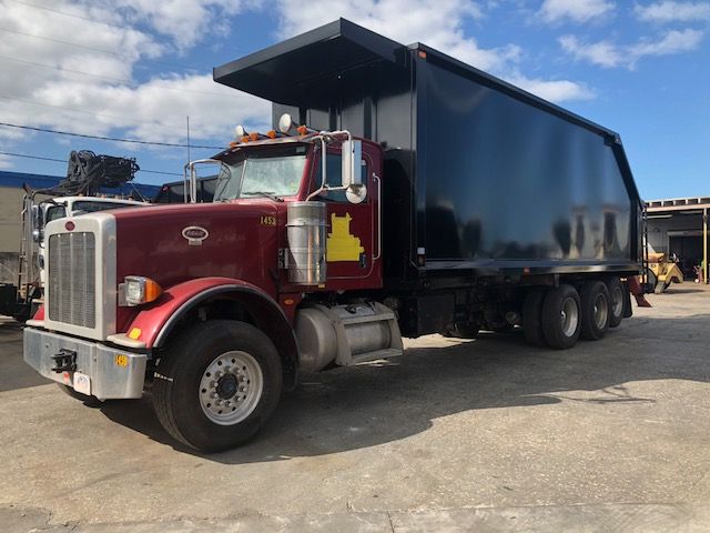 Peterbilt 388 dump truck with maroon cab and black dump body, side view showing large exhaust stacks and chrome bumper.