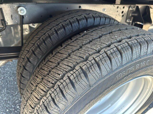 Tire and wheel of a Ford Transit 350 box truck showing tread pattern and wheel arch. Partial undercarriage and frame visible.