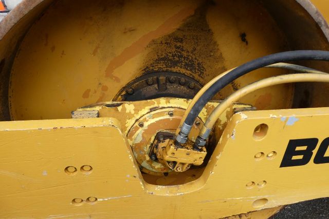 Bomag BW212D-2 drum compactor wheel hub with hydraulic lines and yellow painted metal housing.