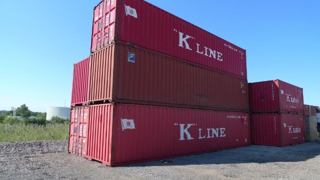 Two stacked red 40' cargo containers with white 'K LINE' lettering, other containers in background, outdoor yard setting.