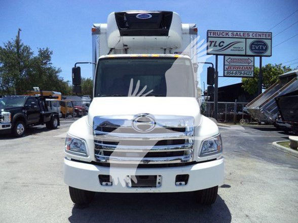 Front view of a white 2019 refrigerated truck with a large grille and a refrigeration unit on the cab roof, dealership lot in background.