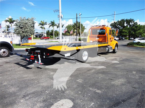 Peterbilt 337 flatbed tow truck with yellow bed and orange cab, side view showing rear hitch and platform.