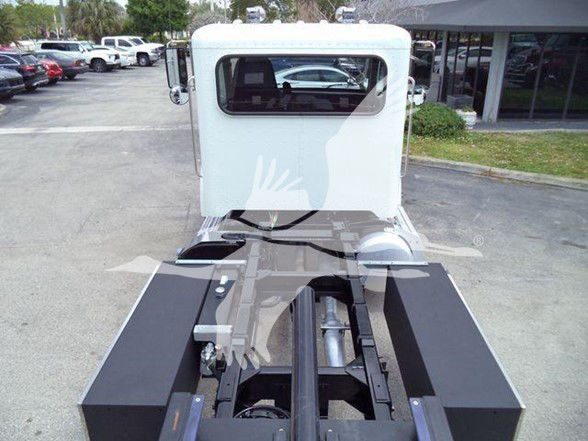 Peterbilt 337 truck cab and chassis in a parking lot, rear view showing frame rails and cab window.