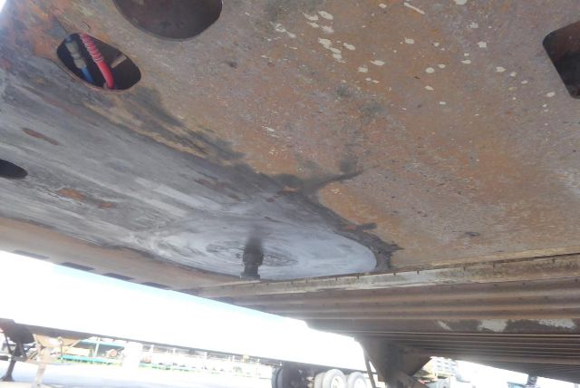 Underbody of a used trailer showing rusted floor and some paint wear, with a wheel and support structure visible in the background.