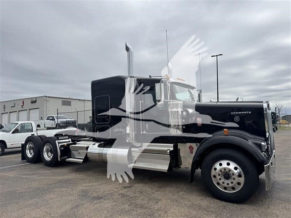 Kenworth W900L conventional sleeper truck showing chrome fuel tanks and dual rear axles in a dealership lot.