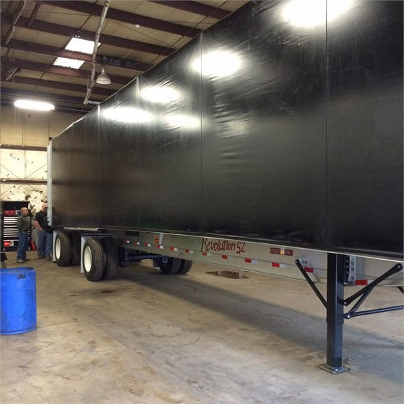 Fontaine tarp system trailer in a workshop with black tarp covering cargo area; ledger reads 'Revolution 52' on side rail near landing gear; inside a facility with workers and tools.